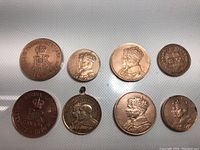 Eight copper-toned coins and one medallion arranged on a white surface, showing both sides and variety of portraits, monograms and crowned crests.