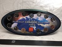 Full front view of the oval Millennium Canada coin display set showing 14 coins around the edge and decorative background with text.