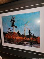 Front view of the framed fine art print featuring a colorful landscape with silhouetted trees and rocky terrain under a blue sky.