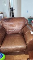Front view of a brown leather stuffed armchair with wide cushioned arms and creased leather seat and back cushion.