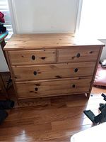 Front view of the wooden chest of drawers showing five drawers and dark metal recessed handles.