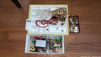 Full view of yellow and white trays containing mixed necklaces, earrings, and other jewelry items along with a box filled with additional pieces.