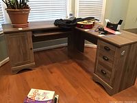 Full view of the L-shaped corner desk showing the wood finish, cabinet, and drawer sections.