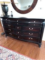 Full view of the dresser showing the front with drawers and hardware, lamp and mirror above, and floor rug.