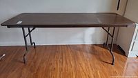 Full side view of metal folding table with four legs and woodgrain tabletop