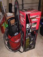 The Husky 1750 PSI power washer next to its original box in a garage setting.