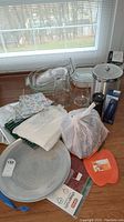 Photo of all items including ice bucket, casserole dishes, pitchers, pizza pan, cutting boards, cloths, and kitchen accessories arranged on a surface in front of a window.