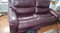 Front view of burgundy leather recliner loveseat on hardwood floor, showing two seat cushions, armrests, and backrest.