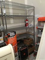 Front view of tall metal shelving unit with six wire shelves, some items like fire extinguisher and boxes around but not included.