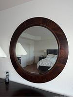 Front view of the round wall mirror hung on a white wall, showing the brown wood frame and clear reflective glass surface.