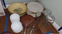 Photo showing assortment of white plates, Corelle bowls, large yellow bowl with design, brown lidded pottery piece, and several clear glass vases.