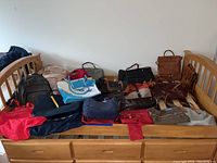 Full view of bags and purses on wooden bed frame showing variety of colors, materials, and sizes