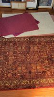 Photo showing four throw rugs stacked with one ribbed dark red rug, a cream/beige rug, and two oriental-style rugs visible.