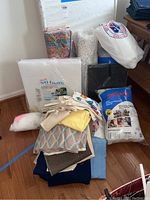 Wide shot showing all items in the lot including white Nu-Foam fiberfill, Poly-Fil bags, colorful fabric bolt, and folded fabric pieces.