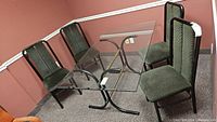 Four metal framed chairs arranged around a glass dining table. One chair has visible seat damage.