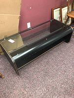 Full side view of the black composite coffee table showing the glass top and rounded edges.