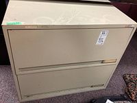 Front view of beige metal two drawer horizontal filing cabinet with visible surface wear and locked top drawer.