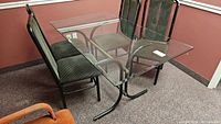 Glass rectangular table with metal curved base and four cushioned dining chairs around it