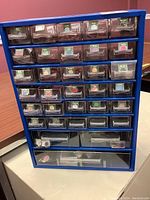 Full view of blue metal hardware organizer with 30 clear plastic drawers containing various small golf ball magnetic markers.