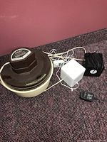 Three humidifiers laid on carpet: one large Cool Mist Humidifier brown color and two smaller Sunbeam humidifiers black and white with cords and remote