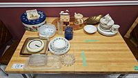 Overview of the kitchenware items on a wooden table including plates, bowls, cups, clocks, and tins.