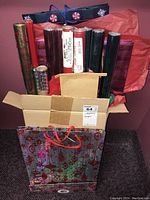 Box filled with assorted rolls of wrapping paper with gift bags in front and beside the box, showing variety and quantity.