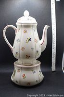 Porcelain coffee pot shown atop matching warmer base with measuring tape to indicate size.