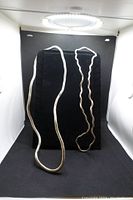 Three silver-colored necklaces displayed on a black background, showing different thicknesses and flexible styles.