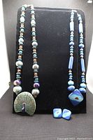Two artist-created clay bead necklaces displayed on black velvet stand along with pair of matching clay earrings in front.