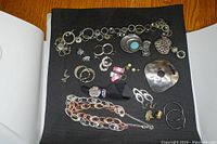 Top view of assorted fashion jewelry on black background including necklaces, rings, earrings, and scarf slides.