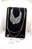 Lot of fashion jewelry displayed on a black stand featuring two necklaces, a pendant, pair of hoop earrings and a pair of stud earrings on a card.