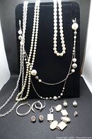 Lot of vintage and contemporary fashion jewelry items displayed on black jewelry stand and surface including necklaces, earrings, and bracelets.