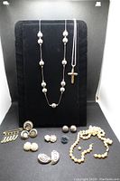 Front view of necklaces hanging on black display stand, several earrings, pin, and ring arranged at the base