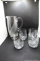 Glass pitcher with four matching glasses in front of black background showing set.