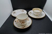 Photo of two tea set groups showing cups and saucers with gold floral pattern on white china