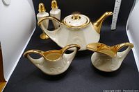 Full set showing teapot, creamer, sugar bowl, salt and pepper shakers on black background with measuring ruler