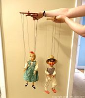 Photo of two marionette puppets held up by strings showing their detailed faces and full outfits.