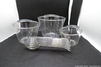 Three clear plastic measuring cups of different sizes and set of five clear plastic measuring spoons with black measurement markings arranged for display.