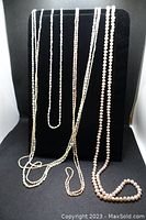 Photo of six pearl necklaces hanging against black background. Mixture of white and light pink pearls, varying sizes and medium to long lengths.
