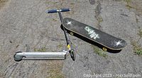 Razor scooter foldable with blue handle grips and black skateboard with 'No Rules' design underneath laid on pavement