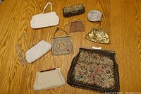 Overview of 9 vintage handbags of varying sizes and materials displayed on wood surface.