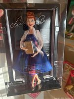 Barbie doll in original packaging showing Lucille Ball Tribute design, doll in navy blue dress with lace shrug holding a book.