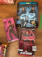 Collector Barbie dolls of Catwoman, Black Widow, and The X-Files Ken & Dana in original packaging, displayed on wooden floor.