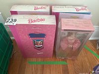 Four Barbie boxes displayed on floor, showing the collector series, with one doll visible inside packaging.