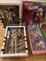 Grouped view of four boxed Barbie dolls: two Stripes HBC, one School Spirit and one Travel Train Fun.