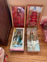 Four boxed international-themed Barbie dolls including a Lunar New Year Barbie, Cambodian Barbie, Princess of the Pacific Islands Barbie, and a Guo Pei designed doll, arranged on wooden floor.