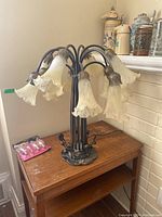 Side view showing the lamp with the multiple flower-shaped glass shades and extra bulbs on table.