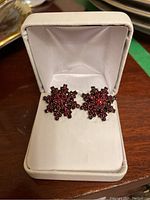 Pair of garnet cluster clip-on earrings displayed in a white jewelry case against a wooden surface.