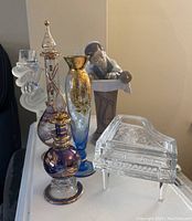 Photo showing the Lladró figurine, two decorative perfume bottles, two vases, and the glass piano-shaped candelabra on a white surface.