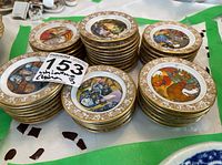Several stacks of miniature round porcelain plates about 3 inches diameter, each plate decorated with colorful fairy tale illustrations and a 22kt gold painted ornate border.
